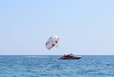 Parasailing su eğlencesi. Tatil köyünün deniz kenarında bir yaz tatilinde bir teknenin arkasında paraşütle uçmak. Tekirova, Antalya Türkiye. 23 Eylül 2020
