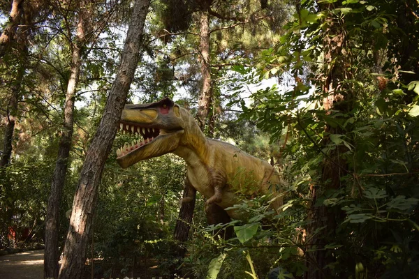 자연적으로 공원에 조각상을 배경으로 굶주린 커다란 티라노사우루스 렉스의 현실적 모델이죠 — 스톡 사진