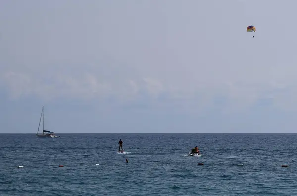 海でのフライボードライダーのシルエットと水平線上の海とセーリングボートの上に青い空にパラセーリング 水のジェットパックを使用しています 極端なウォータースポーツの概念 ジェットスキー動力フライボード — ストック写真