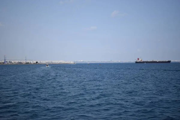 Cargo ship in calm blue Mediterranean in Anatalya. Traveling along the Mediterranean Sea, view of the rocky coast of Antalya. In the distance, cargo ships are visible.