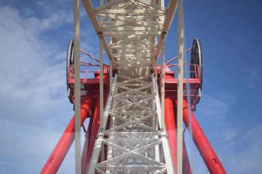 Kulübelerin birinden dönme dolap inşaatı görünüyor. Cazibenin beyaz metal yapısının bir parçası. Dönme dolap iç yapı beyaz bulutlu mavi gökyüzüne karşı