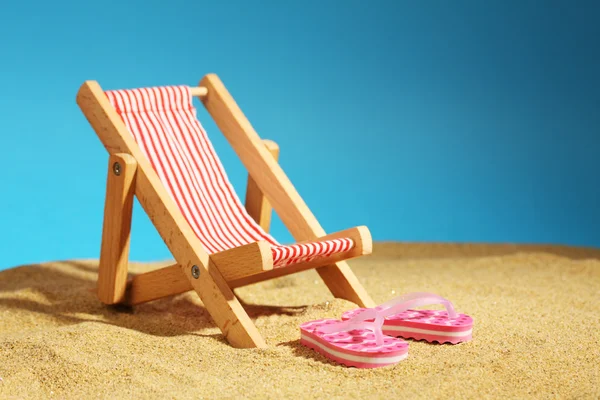 Stripy (vermelho e branco) cadeira de praia de verão e dois chinelos rosa com pontos na areia e céu azul Imagem De Stock