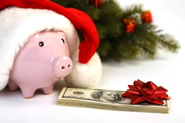 Součástí prasátko s santa claus klobouk a hromadu peněz amerických sto dolarové bankovky s červenou stuhu a vánoční strom stojící na bílém pozadí Stock Snímky
