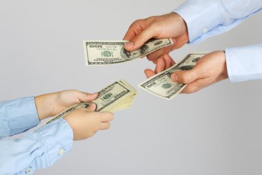 Men's hands give money american hundred dollar bills to boy hands. Businessman give money to business boy. Father and son. clipart