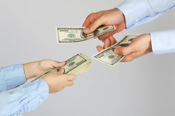 Men's hands give money american hundred dollar bills to boy hands. Businessman give money to business boy. Father and son. — Stock Photo, Image