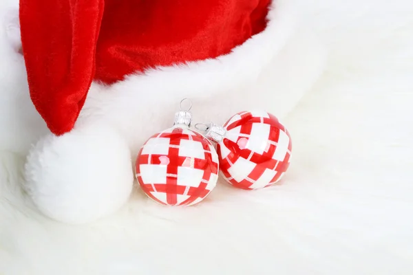 Parte del cappello di Babbo Natale con pom-pom e due palline di Natale rosse e bianche su pelliccia bianca — Foto Stock