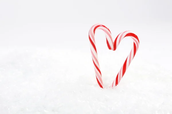 Dois bastões de doces vermelhos e brancos em forma de coração na neve — Fotografia de Stock