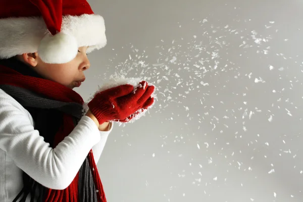 Niño en Santa Claus sombrero y bufanda y guantes soplando copos de nieve —  Fotos de Stock