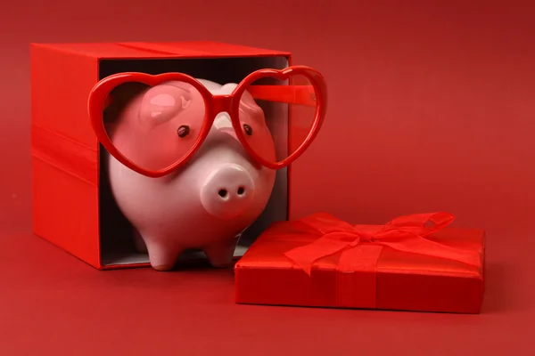 Piggy bank in liefde met rood hart zonnebril permanent in geschenkverpakking met lint op rode achtergrond — Stockfoto