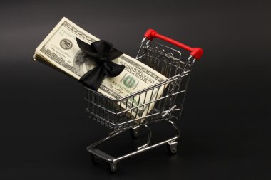Alışveriş sepeti ile para Amerikan yüz dolar faturaları içinde duran siyah arka plan üzerine siyah fiyonklu yığını