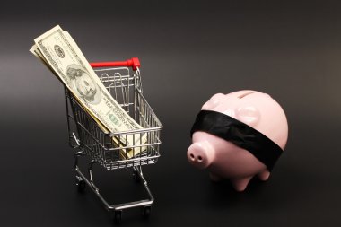 Alışveriş sepeti içinde para Amerikan yüz dolar faturaları yığını ile ve pembe kumbara - yatay siyah arka plan üzerinde siyah gözleri bağlı duran ile