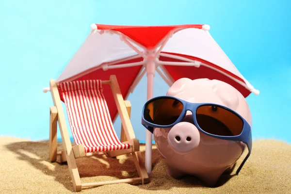 Sommer-Sparschwein mit Sonnenbrille steht auf Sand unter rot-weißem Sonnenschirm neben Strandkorb — Stockfoto