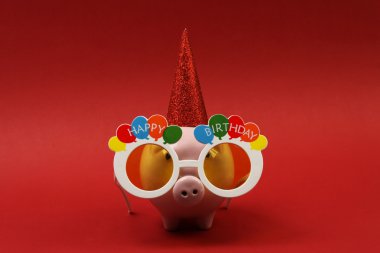 Güneş gözlüğü mutlu doğum günü, parti şapkası kırmızı arka plan-yatay üzerinde ile Piggy banka