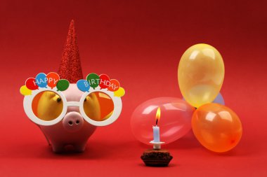 Güneş gözlüğü mutlu doğum günü, parti şapkası ve çok renkli parti balonu ve doğum günü pastası ile kırmızı arka plan-yatay üzerine de mum ile Piggy banka