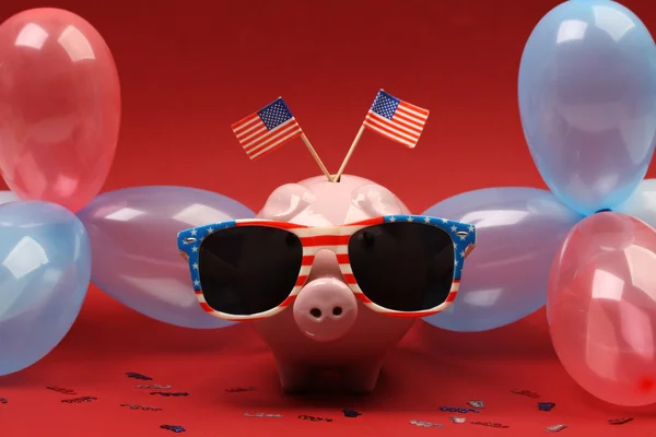 Piggy bank with retro sunglasses with USA flag and blue, red and white party balloons and two small USA flags on red background — Stock Photo, Image