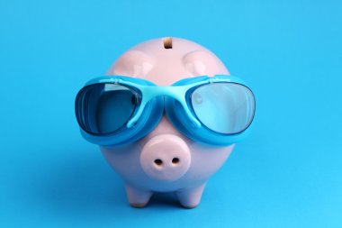 Pink piggy bank with blue swimming goggles on blue background like swimmer clipart
