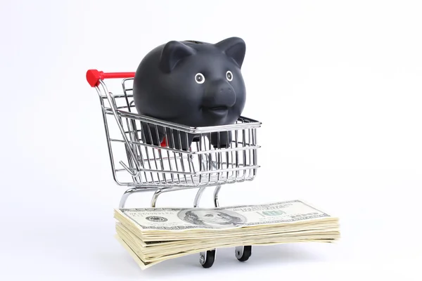 Shopping basket with black piggy bank and stack of money american hundred dollar bills on white background — Stock Photo, Image