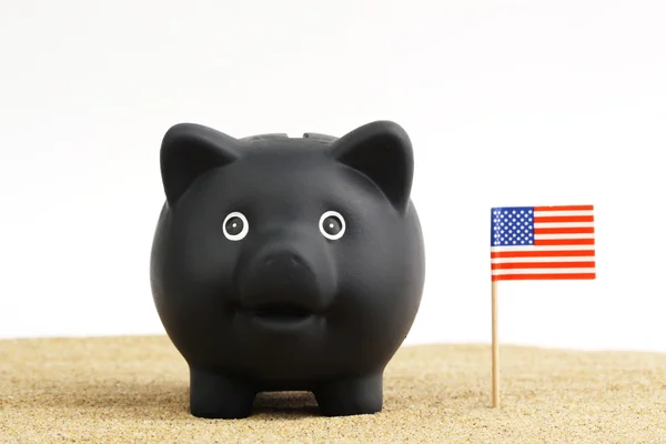 Zwarte piggy bank staande naast Usa vlag op zand voor witte achtergrond — Stockfoto