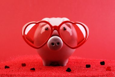 Kırmızı kalp güneş gözlüğü ile aşk piggy banka içinde kırmızı kum üzerinde kalp pırıltılar kırmızı arka plan önünde parlayan kırmızı ile ayakta düşmüş
