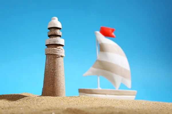 Lighthouse on sea sand, sailboat and blue sky — Stock fotografie