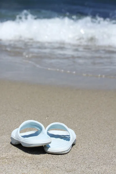 Синие шлепанцы на песчаном пляже перед морской волной — стоковое фото