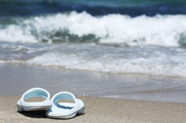 Dalga deniz önünde kum plajı üzerinde mavi flip flop