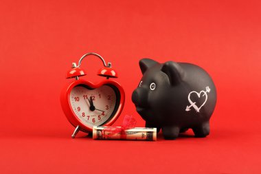 Beyaz kalp ve kalp çalar saat ve Hediyelik para Amerikan yüz dolar faturaları ile kırmızı bir arka plan üzerinde kırmızı kurdele duran siyah kumbara