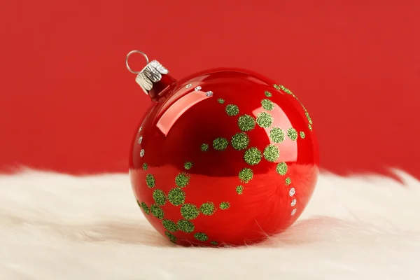 Boule de Noël rouge brillante avec étoiles vertes sur fourrure blanche devant fond rouge — Photo