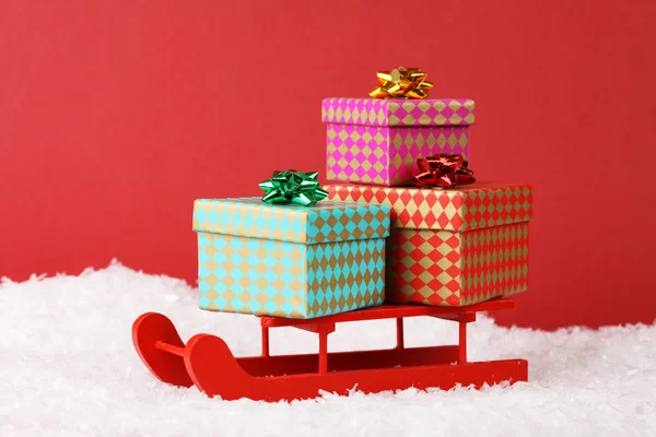 Tres cajas de regalo con lazo en trineo rojo sobre nieve sobre fondo rojo — Foto de Stock