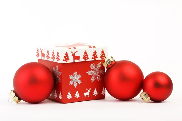 Red christmas box with red Christmas decoration and three red matt christmas balls on white background.  Christmas box with christmas tree and reindeer and silver glitter snow flakes. — Stock Photo, Image