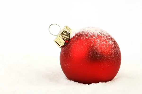 Boule de Noël rouge enneigée mat debout sur la neige sur fond blanc — Photo