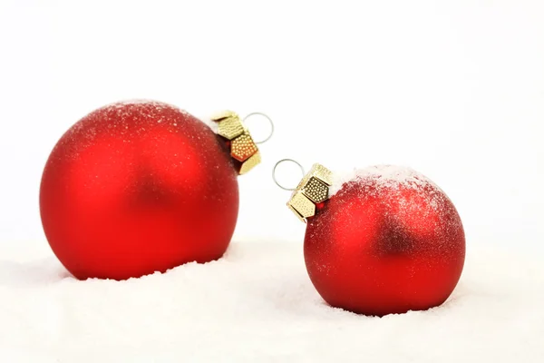 Deux boules de Noël rouges enneigées mat debout sur la neige sur fond blanc — Photo