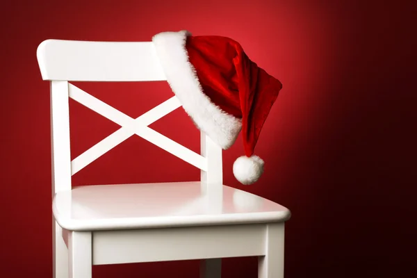 Klobouk Santa na bílé židle před červeným pozadím Stock Obrázky