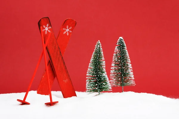 Красные лыжи с палками лыжи и два снежных дерева на снегу на красном фоне — стоковое фото