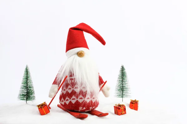 Christmas helper (elf) skiing on snow next two snowy trees and three gifts  Red and white colors — Stock Photo, Image