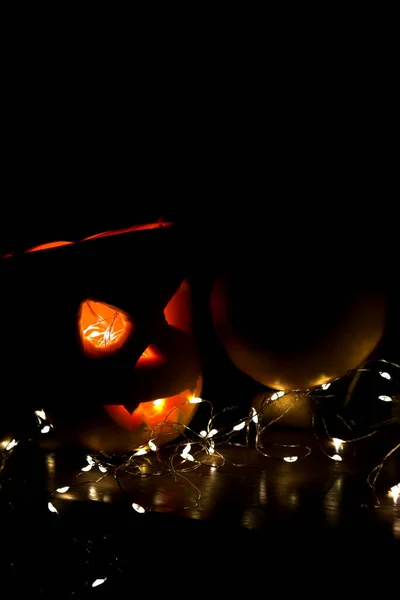 Carved pumpkin illuminated from the middle lies in the dark. Next to the pumpkin is another garland that illuminates it