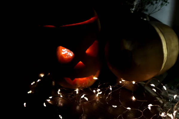 Carved pumpkin illuminated from the middle lies in the dark. Next to the pumpkin is another garland that illuminates it