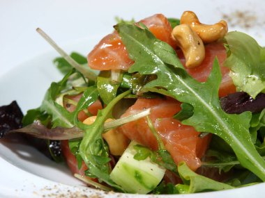 Arugula salatası, somon, avokado, fesleğen ve beyaz tabakta kaju..