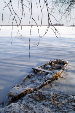 Kıyıya yakın buzda donmuş karla kaplı eski ahşap bir tekne..
