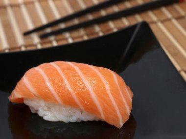 Siyah tabakta somon balıklı suşi ve bambu hasırı..