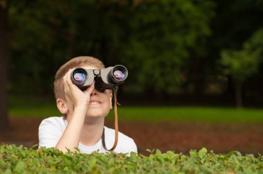 Dürbünlü çocuk çalıların arkasına saklanıp birini izliyor.