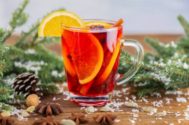 Bir bardak sıcak Noel şarabı, portakal dilimi ile süslenmiş, anason ve tarçın çubukları ladin dallarının yanındaki ahşap masada.