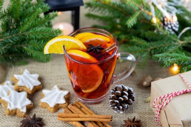Bir bardak sıcak şarap, şarap, punç, taze portakal dilimleri ve tarçın çubuğuyla süslenmiş Noel kurabiyelerinin yanında bir ağaç, hediyeler. Sıcak kış içeceği