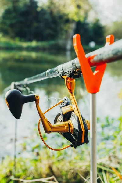 Fishing and recreation concept. Hobby in nature. Close-up of a fishing rod or spinning rod with a reel on the lake. Vertical orientation.