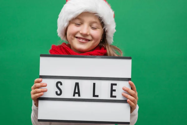Verkoop, Kerstmis en Nieuwjaar winkelen. Een schattig blank meisje met een kerstmuts met een verkoopbord. Een close-up. Online winkelen tijdens kortingsperioden. — Stockfoto