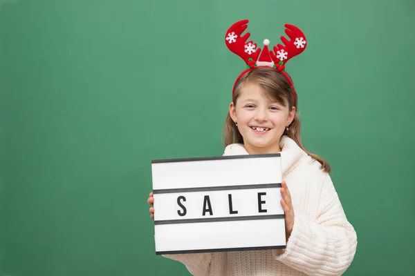 Verkoop, Kerstmis en Nieuwjaar winkelen. Schattig blank meisje met een kerstrendier gewei en een uitverkoop bord in haar handen. Groene achtergrond, plaats voor tekst. Online en internet winkelen — Stockfoto