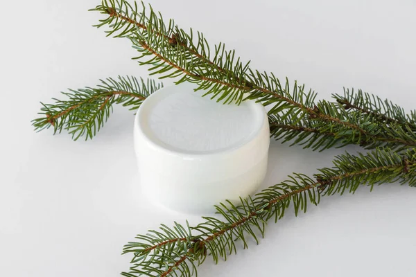 Organik kozmetik ürünleri. Yeşil ladin, çam ve köknar dallarının yanında krema ya da losyonlu beyaz kavanoz. Alay et. Biyolojik doğal vücut ve yüz bakımı.