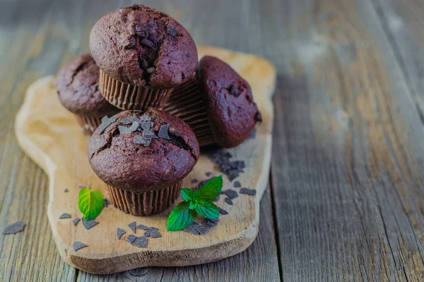 Färska hemgjorda chokladmuffins eller cupcakes på en träskiva på en rustik trä bakgrund med färska gröna mynta blad. Plats för ditt sms. Bageri, bageri — Stockfoto