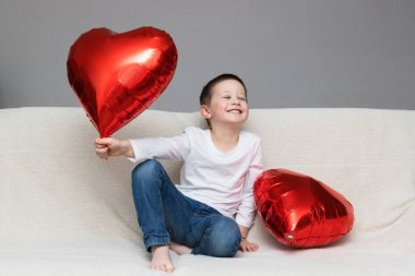 Sevgililer Günü konsepti. Kırmızı balonlu beyaz çocuk kanepede keyif çatıyor. Mesajın için yer aç. Neşeli bir aşk tatili