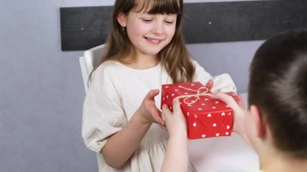 Şirin bir çocuk koyu saçlı tatlı bir kıza hediye kutusu veriyor. Kalpli güzel kırmızı kutu. Yavaş çekim. — Stok video